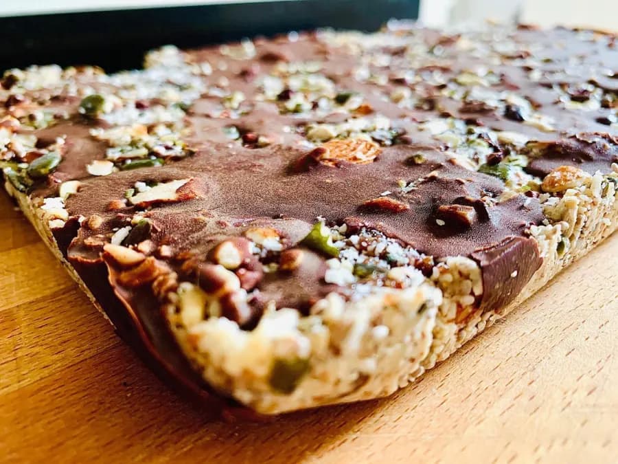 A tray of Bodhi Flapjack raw energy bars on a wooden board, topped with raw chocolate, nuts and seeds