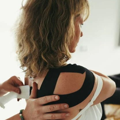 Kinesiology tape being applied to a client’s shoulder by an injury specialist